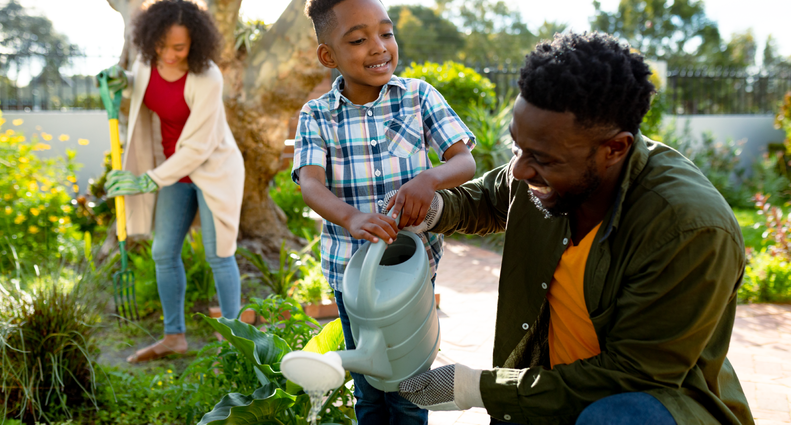 a parent helps child water plants with a watering can