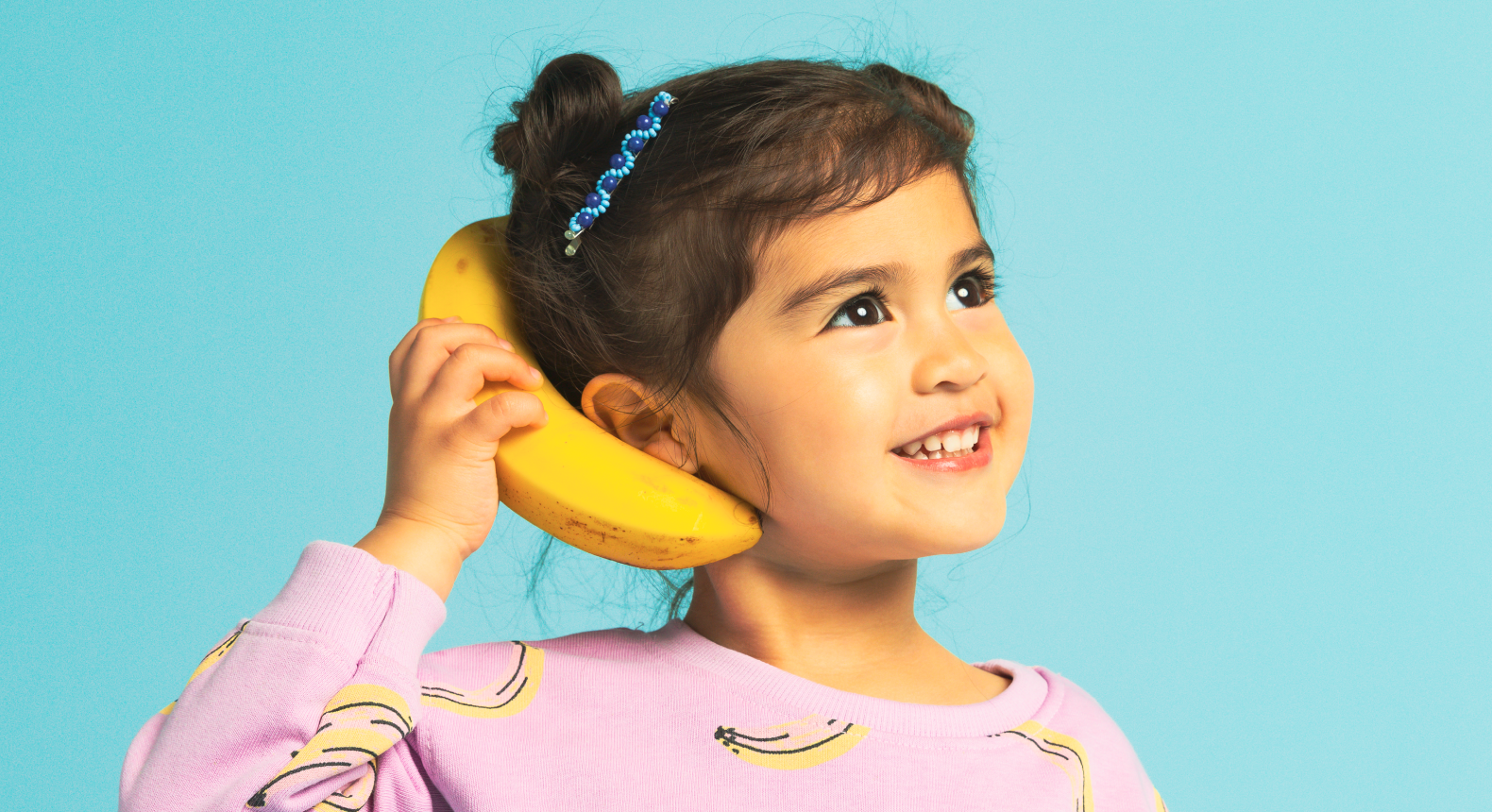 a child holding a banana like it's a phone on a blue background