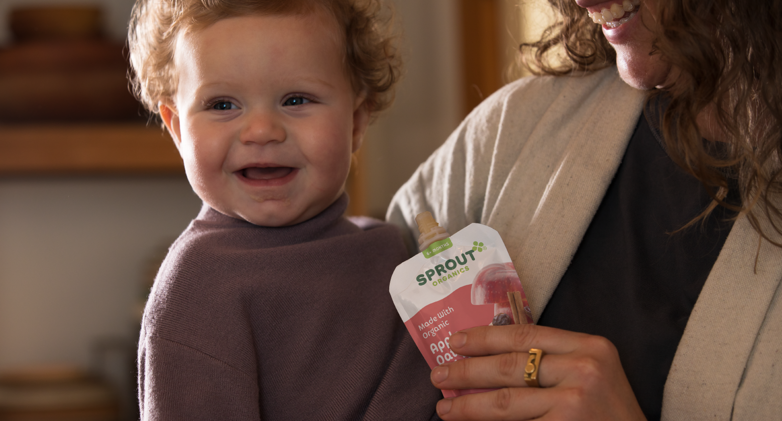 child with caregiver holding a sprout organics pouch