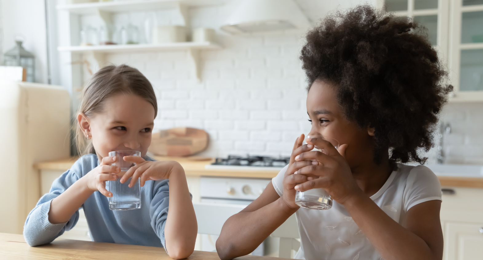 two children in a kitchen drinking glasses of water