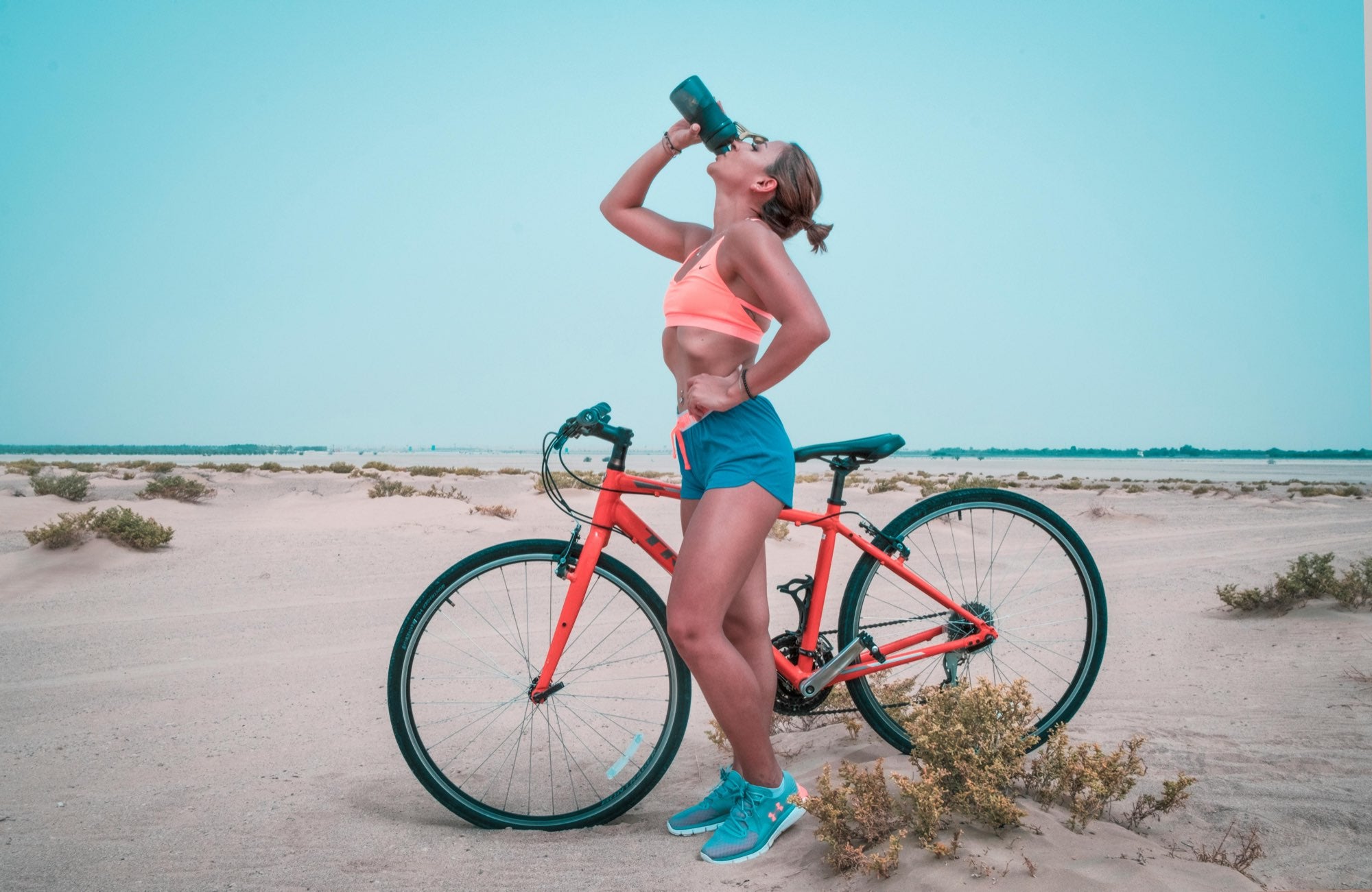 Femme sportive sur un vélo sur la plage qui boit à sa gourde
