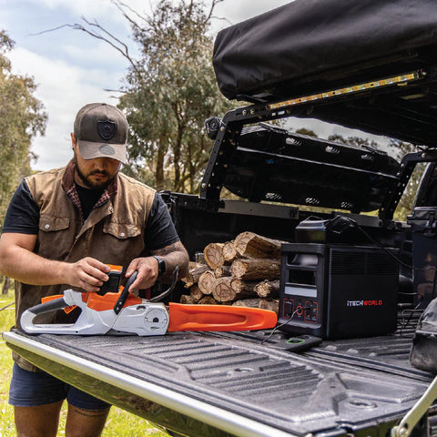 A photo of a man holding a chainsaw which is connected to an iTech PS1400 Power Station inside of a ute.