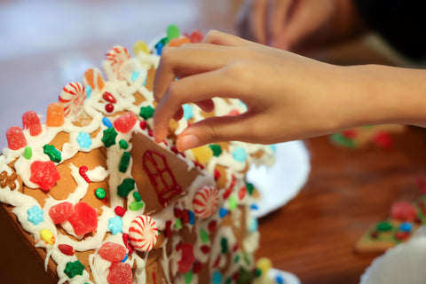 Child's hand applying colourful candies to gingerbread house with royal icing