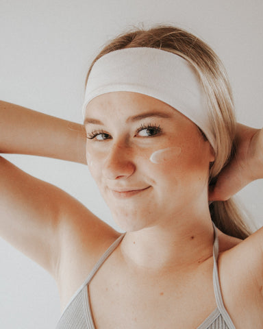 Fair-skinned young woman with smudge of moisturizer on cheek and white headband