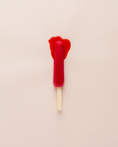 Red ice lolly melting on a light pink background