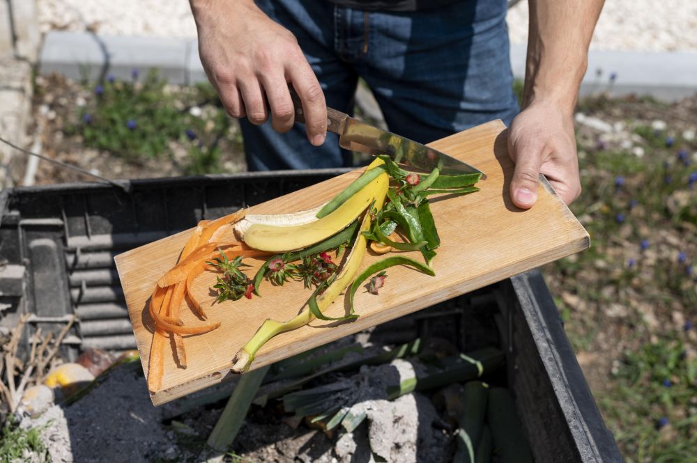 hand-holding-wooden-board-pouring-fruit-peels-into-compost