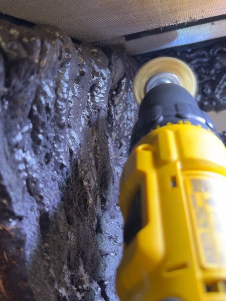 A yellow dewalt drill carving the spray foam background of a bioactive terrarium.