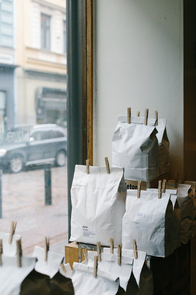 A photograph of white paper bags, sealed with clothespins, stacked on a shop window. 