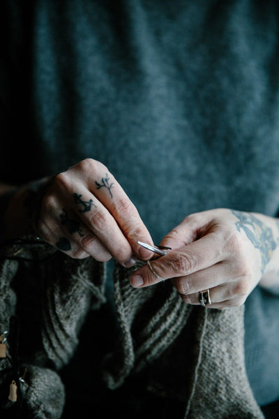 A close-up of tattooed hands knitting.