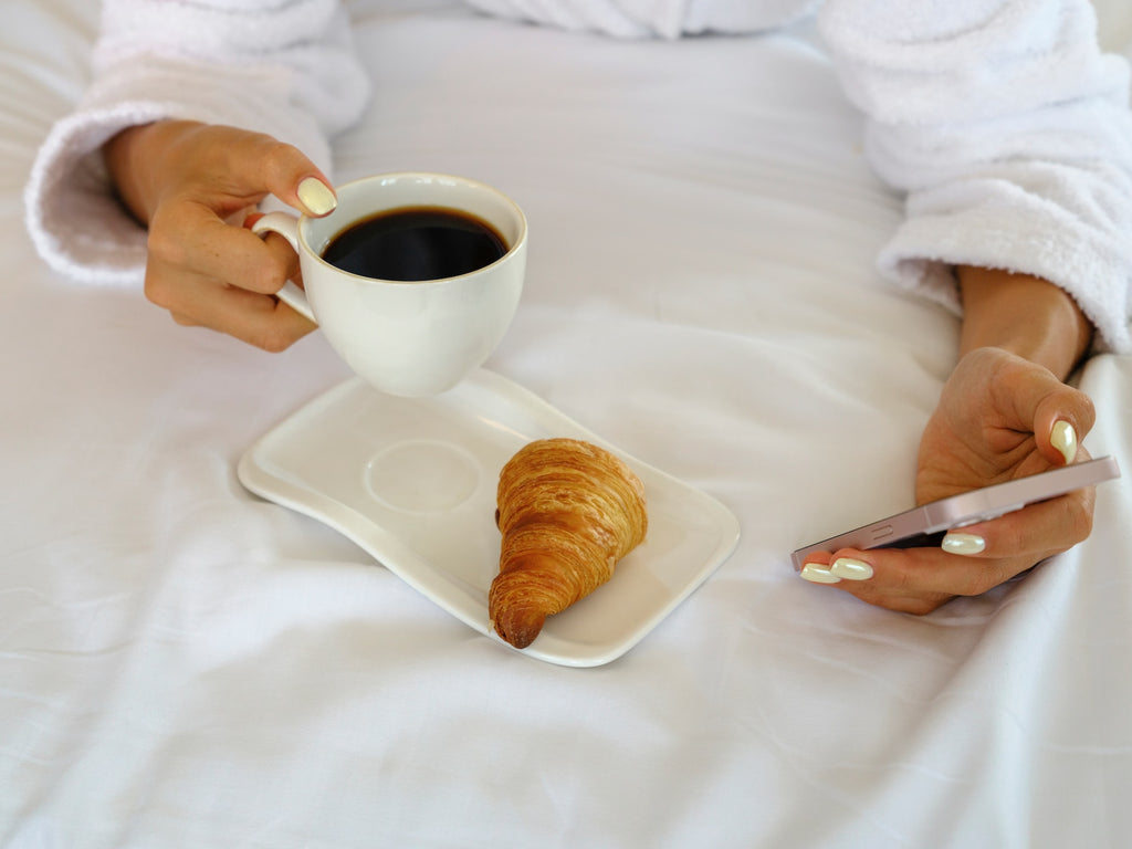 ベッドでスマートフォンとクロワッサンとコーヒー