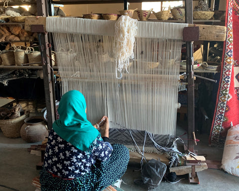 A woman sitting next to a loom and weaving a moroccan berber carpet