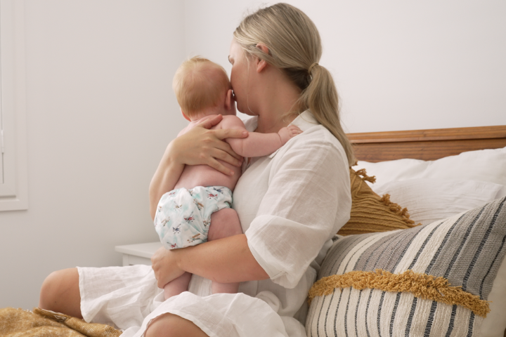 Mother holding baby on bed wearing cloth night nappy