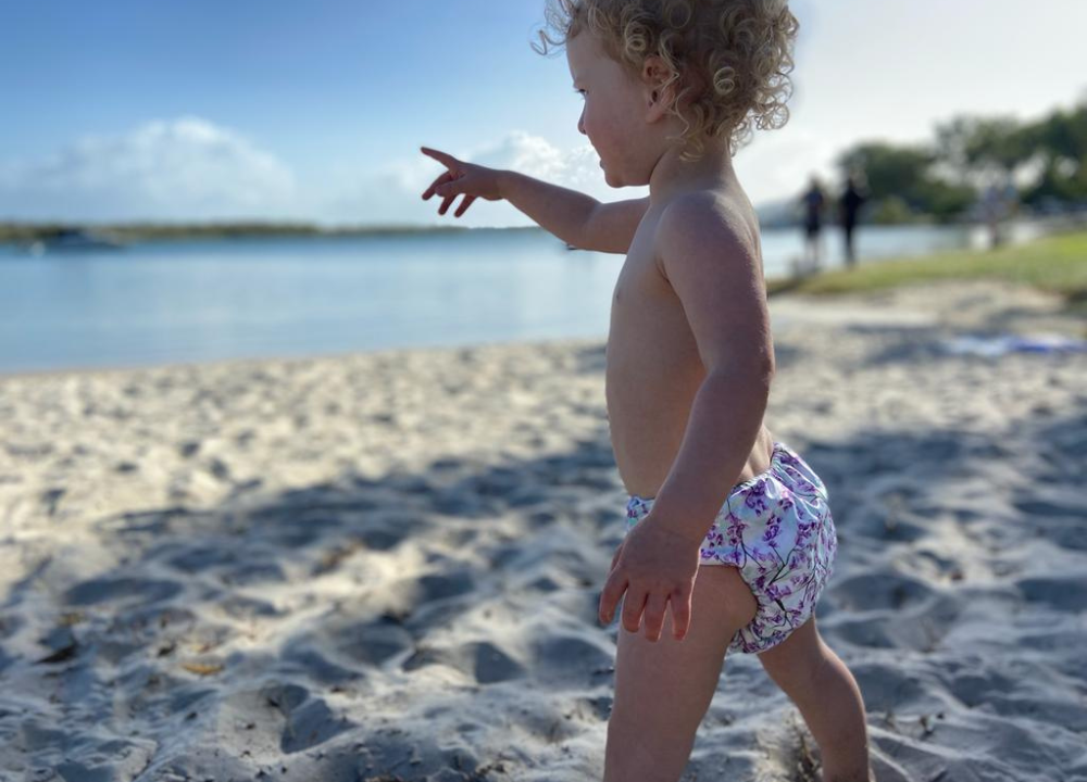 Toddler wearing swim nappy at the beach pointing to the water