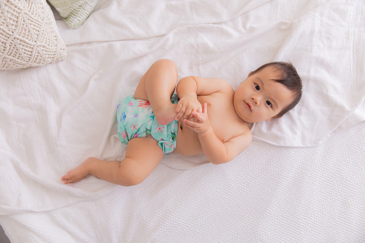 baby on white bed sheets in ocean themed cloth nappy