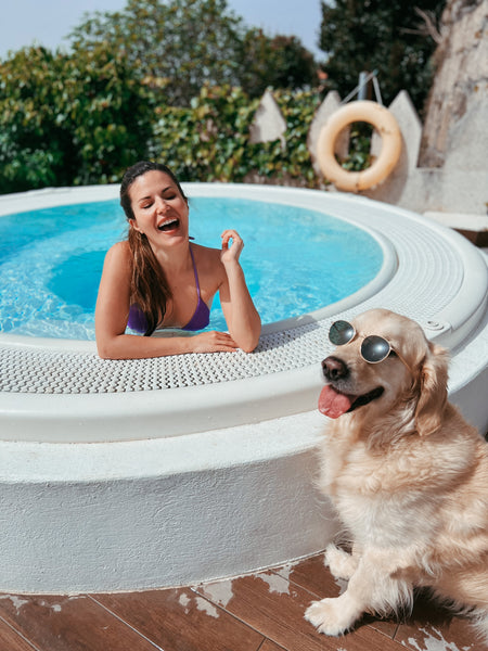Mujer en una piscina con su perro golden retriever que lleva unas gafas de sol y ambos sonríen