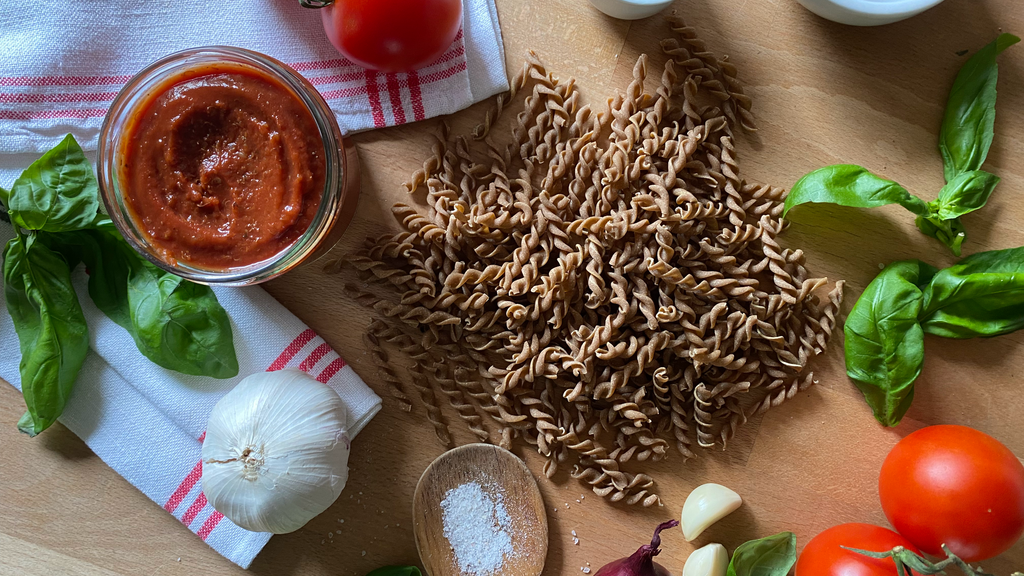 Quinoanudeln mit Zutaten Basilikum, Tomaten, Tomatenmark, Knoblauch und Salz auf einem Holztisch.