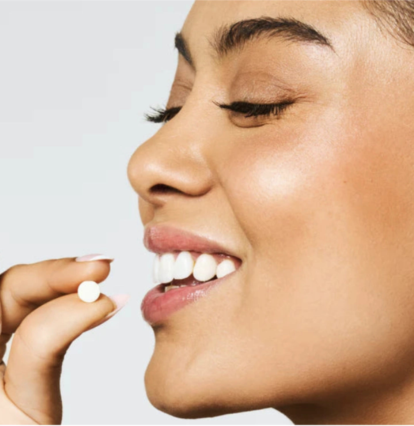 Person smiling, about to take a small tablet.