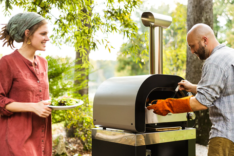 A couple cooking a meal in a Fontana Forni pizza oven while camping