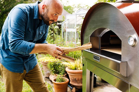 Man fueling a woodfired pizza oven with kiln dried wood