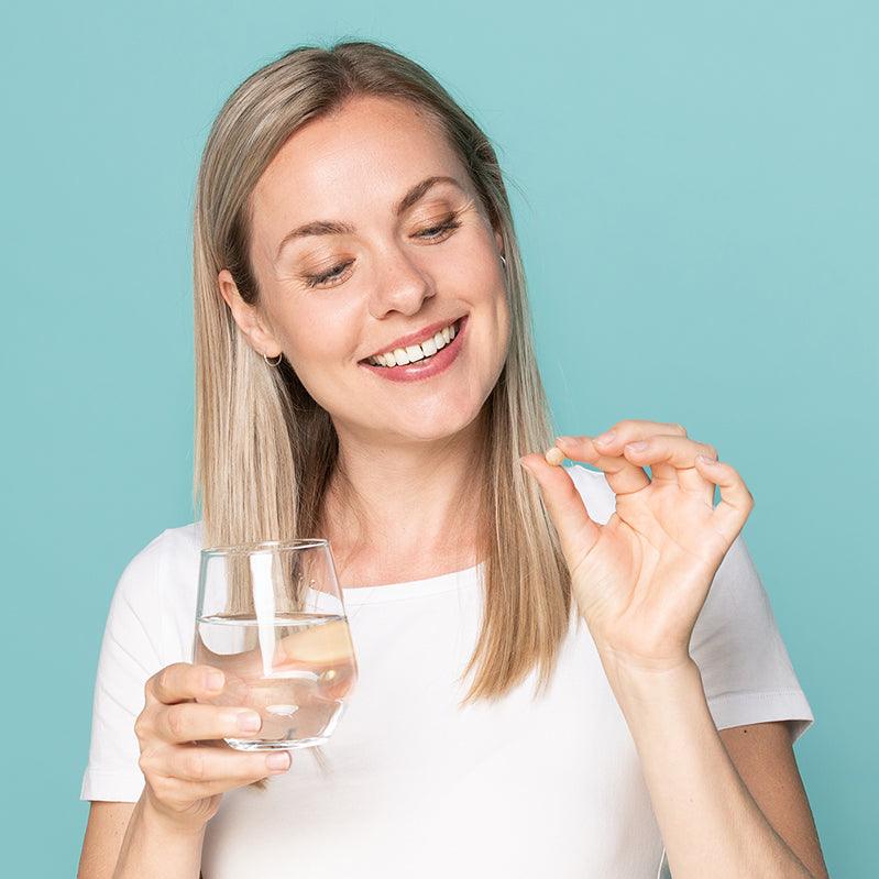 Vrouw met Neofollics hair growth supporting tablets  en een glas water.