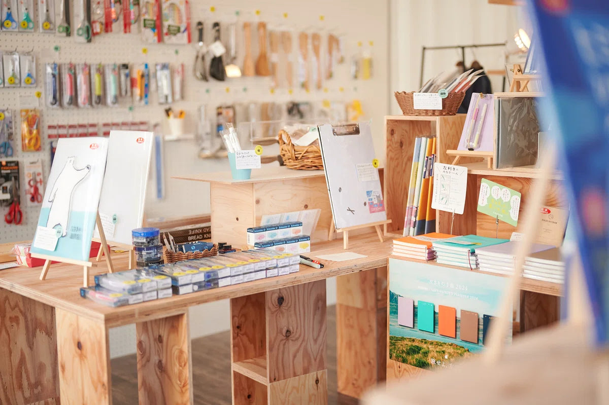 Display of left-handed products at Hidari’s store, featuring stationery, kitchen tools, and other items on wooden tables with a pegboard wall in the background.