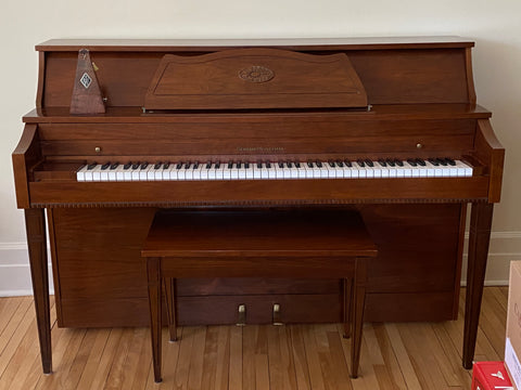 a dark brown wood piano resting on a white wall and sitting on hardwood floors, one of the things that cause a little stress through the move