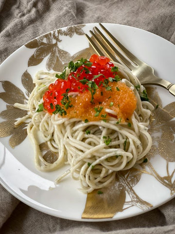Salmon and whitefish caviar over garlic parsley angel hair on a white plate with scalloped edges