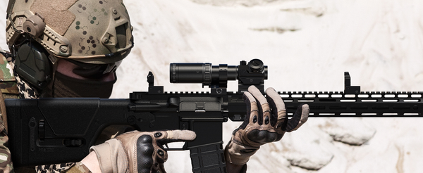 Soldier aiming with a tactical rifle equipped with a precision scope for enhanced targeting in desert terrain.