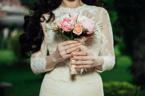 A woman in a bridal dress with a small bouquet of peonies and roses.