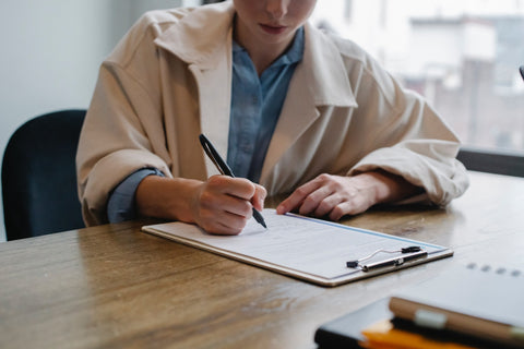 woman writing on a paper in front of a laptop