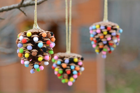 pinecones with multi coloured pom poms stuck into them, hanging on a christmas tree