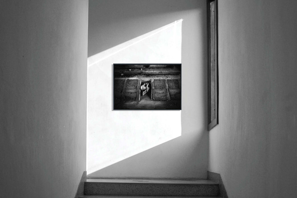 A fine art nude photograph hanging in a staircase next to a window