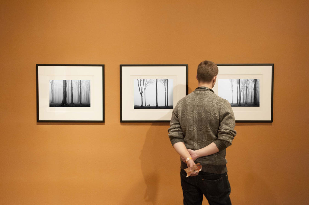 3 artworks hanging on the wall while being viewed by a man