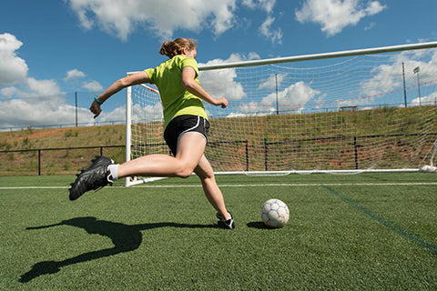 A female athlete kicking a soccer ball into a goal on a practice field.