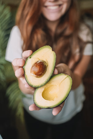 Frau hält eine aufgeschnittene Avocado in den Händen