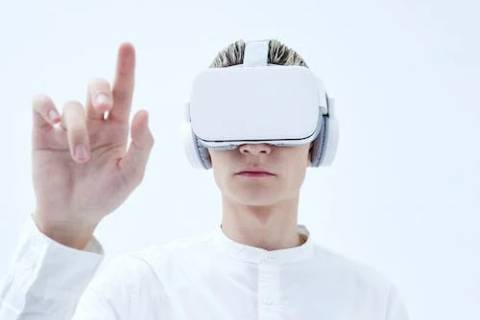 A man using a Virtual Reality headset, holding a finger up.