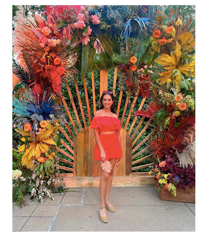 Sareen Sethi in front of flower wall by colonial house of flowers at the Atlanta Botanical Gardens