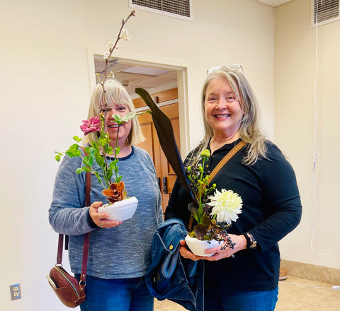 two gray haired ladies holding Japanese ikebana floral art