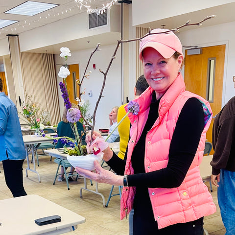 women in pink puffer jacket and pink cap holding a modern ikebana flower arrangement at workshop at museum of art in dothan alabama