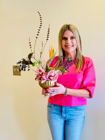 blonde woman in pink shirt holding an ikebana luxury flower design in gold vase