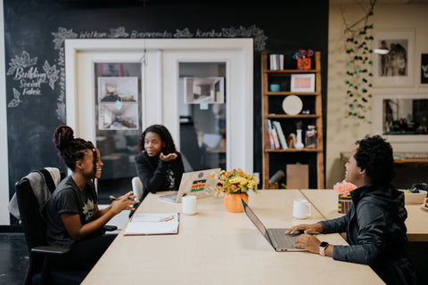 Three young women sitting around a table with laptops and notebooks talking