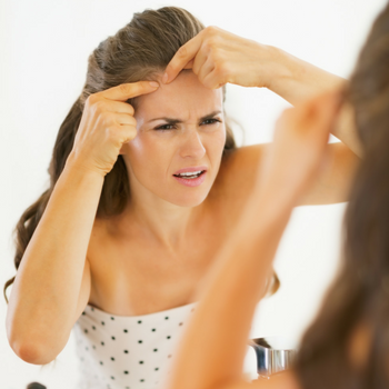 woman popping a zit in the mirror