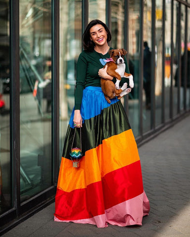woman with green top, full skirt maxi multi coloured skirt and a small dog in hand