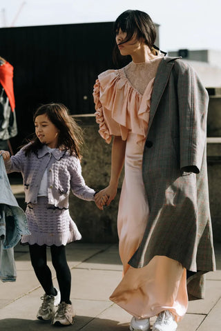 woman with light pink dress holding hands with a little girl