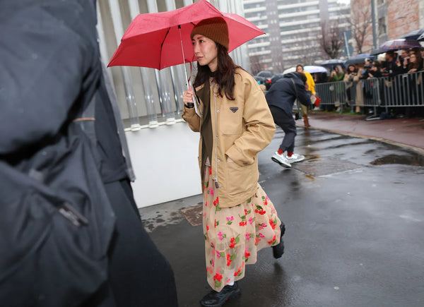 woman holding an umbrella, wearing a sheer skirt with flowers and a Prada beige jacket