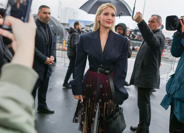 woman with blonde hair wearing a short black blazer with long fringes and a burgundy pair of hotpants underneath