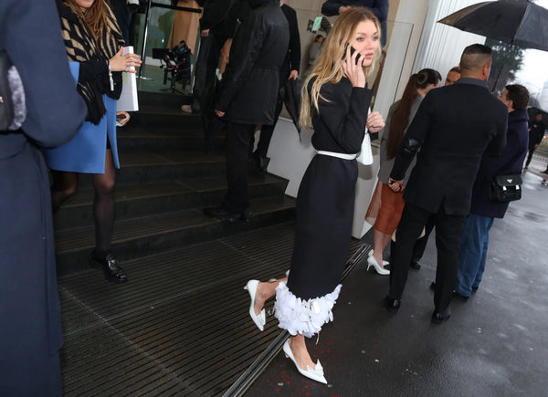 woman talking on the phone, wearing a black dress with white details and white pumps