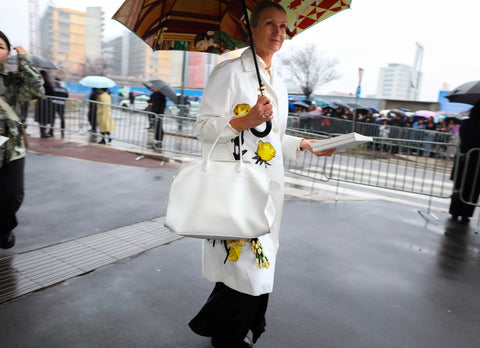 woman wearing a white overcoat with japanese print, holding an umbrella with paintings in its inside