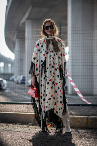 woman holding a red handbag wearing a white long cape with fringes and symbols of cards printed