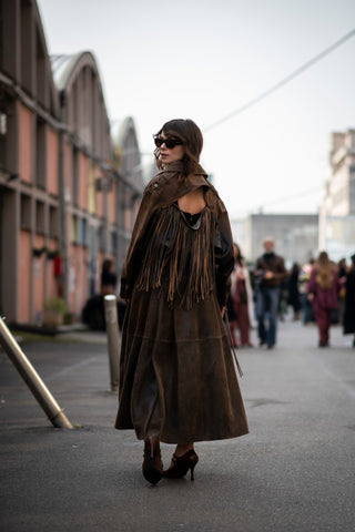 woman wearing a long brown suede coat with open back detail and fringes